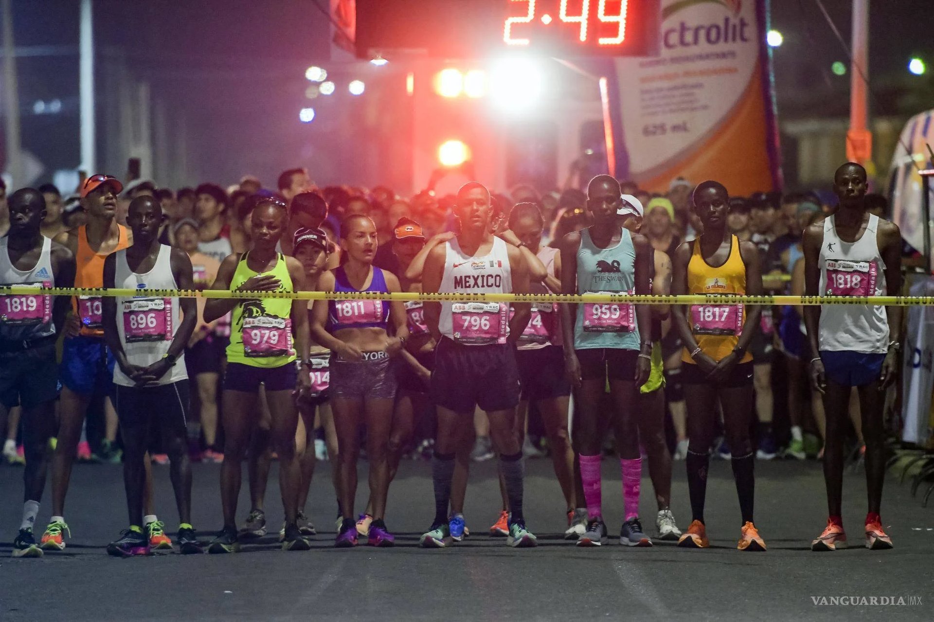 Carrera nocturna con corredores en la línea de salida y cronómetro digital mostrando el tiempo oficial